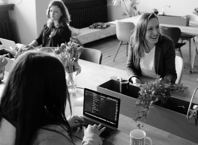 three women sitting at a desk working and having a chat